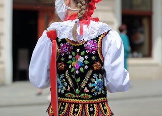 Little blond girl with braid in traditional folk costume from Krakow, Poland, wearing protective facial mask in street