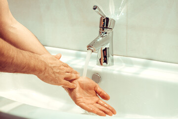 closeup of young caucasian man washing his hands with soap in the sink of bathroom Personal hygiene, protection against viruses and bacteria concept