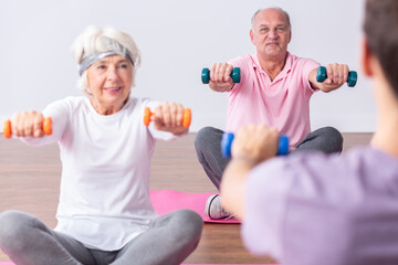 Couple of active seniors during exercises on gym with young instructor