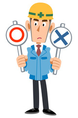 マルとバツの札を両手に持ち考えるヘルメットを被った作業着の男性
