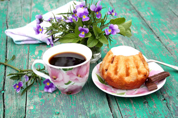 On a green table is a mug and a sweet dessert. Tea party concept in nature. Rum baba on a saucer and a drink in a beautiful mug.
