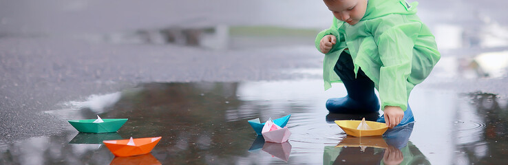 a boy plays boats in a puddle / childhood, walk, autumn game in the park, a child on a walk
