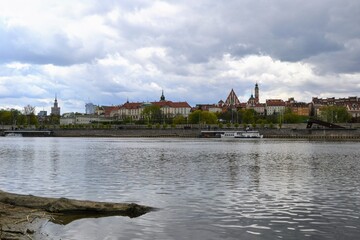 Obraz premium Scenic view of the Old Town - historic quarter of Warsaw with Royal Castle and red roof tenements seen from the Vistula river side. Cloudy day in Warsaw, Poland