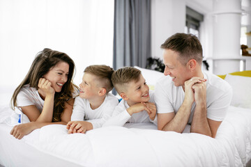 Young family enjoying in bed. Happy parents with sons relaxing in bed.