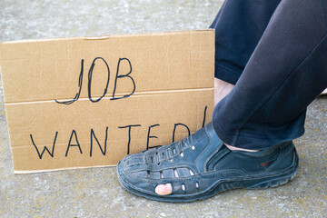 unemployment concept man in old torn shoes sits on a ground at his feet cardboard sign saying job...