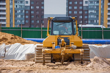 Fototapeta na wymiar Heavy bulldozer back view on the construction of sewage and heating communications under the road, amid multi-story residential buildings.