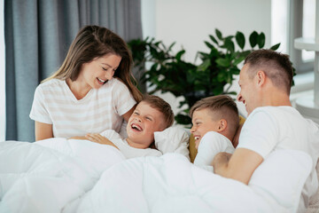 Obraz premium Young family enjoying in bed. Happy parents with sons relaxing in bed.