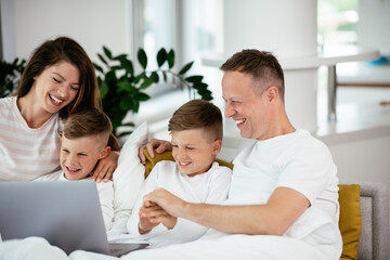 Fototapeta premium Young family watching movie on lap top. Beautiful parents with kids enjoying at home.