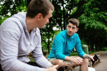 Fit young men taking rest from running. Two friends training outdoors.	