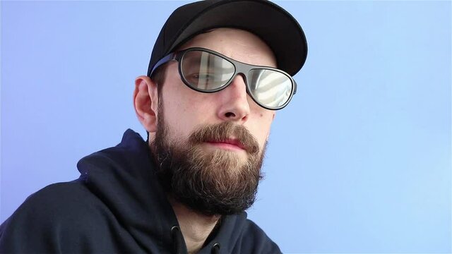 bearded man in cap and hoodie put on sunglasses and look at the camera 
