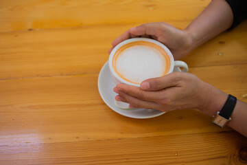 Hand Women put a Latte arts coffe hot coffee on wooden table.barista love art concept.