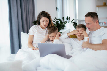 Obraz premium Beautiful parents with kids enjoying at home. Young family watching movie on lap top.