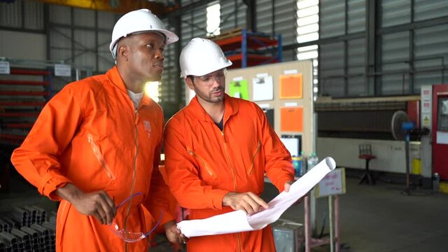 Two workers wearing hard hats speak of factory work.