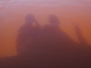 Shadows of people reflected in a slightly reddish-pink lake, Lac Rose, Dakar, Senegal