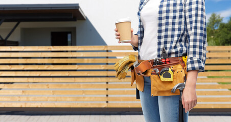 Fototapeta na wymiar repair, construction and building concept - woman or builder with takeaway coffee cup and working tools on belt over living house on background