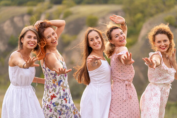 A cheerful company of beautiful girls friends enjoy the company and have fun together in a picturesque place of green hills.