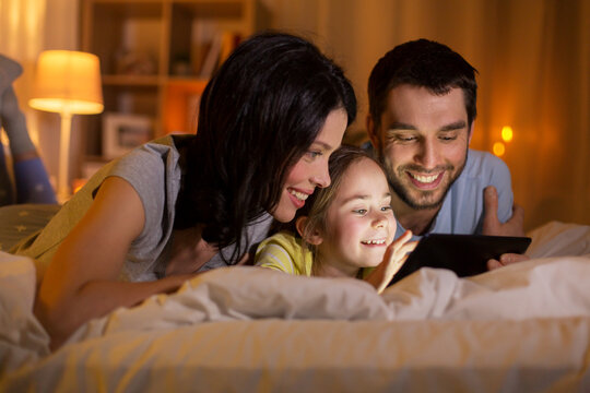 people and family concept - happy mother, father and little daughter with tablet pc computer in bed at night at home