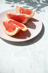 Cut grapefruit slices on pink plate on marble table with selective focus and copy space, vertical. Fresh citrus rich source of antioxidants