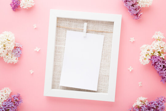 White frame with blank card. Colorful lilac blossoms on light pink table background. Pastel color. Empty place for cute, emotional, sentimental text, lovely quote or positive sayings. Top down view.
