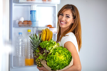 Woman picking up some fruits and veggies from the fridge. Closeup of a cheerful young woman picking...