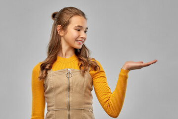 presentation and people concept - happy smiling young teenage girl holding something on empty hand...