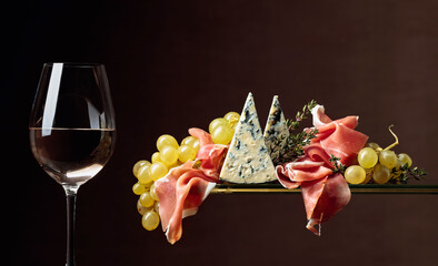 Glass of white wine with snacks. Grapes with blue cheese, prosciutto and thyme.