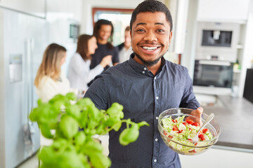 Afrikanischer Mann mit Salat und Basilikum in Küche
