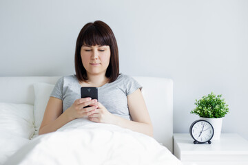young woman using smart phone lying in bed at home