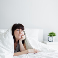 portrait of young woman lying in bed and thinking or dreaming about something at home