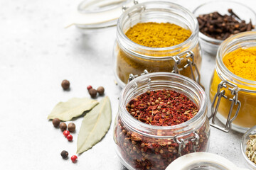 Spices and condiments in glass jars on a light gray table. Spices close-up with space for text