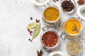 Spices and condiments in glass jars on a light gray table. Spices close-up with space for text. The view from the top
