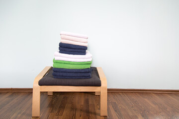 a stack of multi-colored clean towels lies on a textile-wooden stool in the room. light blue wall in the background