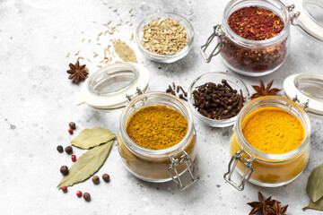 Spices and condiments in glass jars on a light gray table. Spices close-up with space for text. The view from the top
