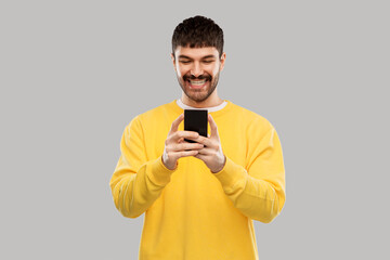 technology, communication and people concept - happy smiling young man with smartphone over grey background