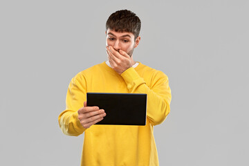 technology and people concept - shocked young man in yellow sweatshirt with tablet pc computer over grey background