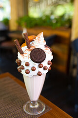 Cool milkshake with cookies and chocolate balls. Milkshake in a glass beaker on a table on a street platform in a cafe. Refreshing summer drinks