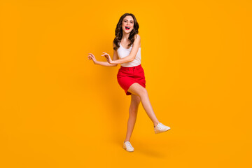 Fototapeta na wymiar Full length photo of amazing cheerful lady walk down street sunny day good mood raise leg hands laughing wear white casual singlet red mini skirt shoes isolated yellow color background