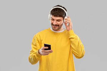 music, technology and people concept - smiling young man with headphones and smartphone over grey...