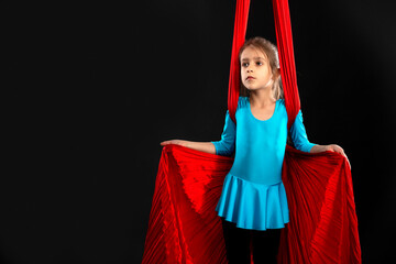 Fearless pretty little girl in a blue gymnastic suit shows a stunt aerial red ribbon on a black...