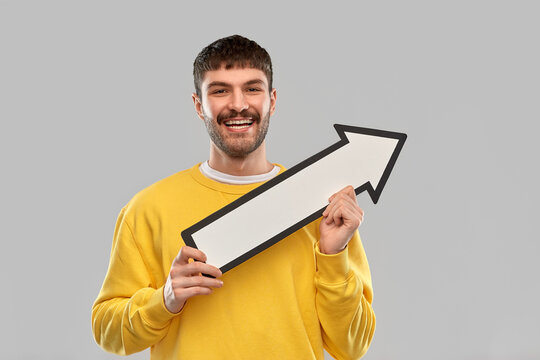 Direction And People Concept - Happy Smiling Young Man Holding Big White Thick Upwards Arrow Pointing To Right Over Grey Background