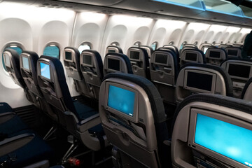 The interior of the aircraft. Empty airplane cabin. Rows of passenger seats with screens in the head restraints