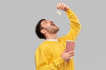 fast food people concept - young man in yellow sweatshirt eating popcorn throwing it to open mouth...