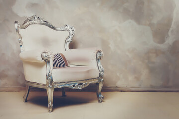 An antique white chair against wall. Antique leather chair. There is striped pillow on chair