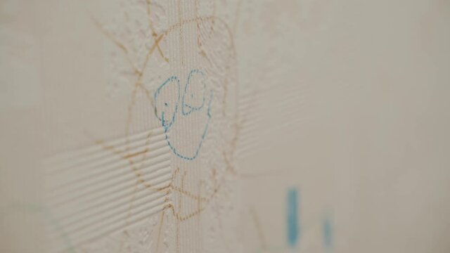 Close-up as a Caucasian boy draws with a marker, felt-tip pen sun eyes and a smile on the wallpaper
