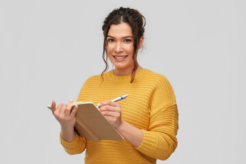 education, inspiration and people concept - happy smiling young woman with pierced nose writing to...
