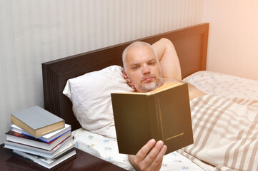 A young man on a Saturday morning reads a book in his bedroom. Self-isolation.