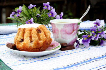 Afternoon tea with rum baba and chocolates on a table in the garden. Dining in the open air. Violet flowers in the background, selective focus.
