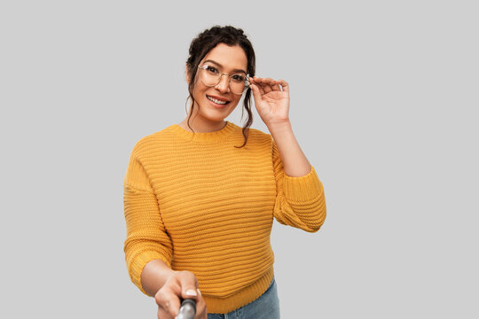 people concept - portrait of happy smiling young woman with pierced nose taking picture with selfie stick over grey background
