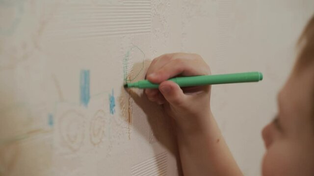 Close-up as a Caucasian boy draws with a marker, felt-tip pen a tree on the wallpaper