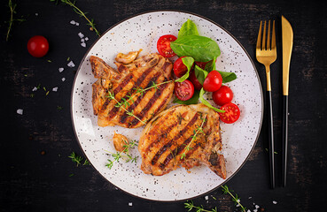 Grilled pork steaks and salad with tomatoes in plate on dark background. Top view, overhead, copy space